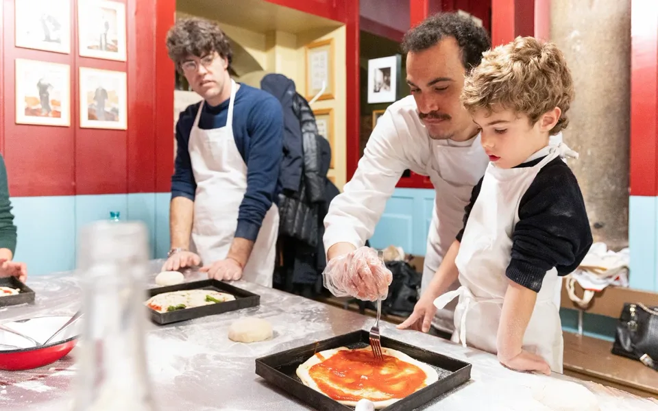 Un istruttore che aiuta un giovane partecipante a preparare la pizza